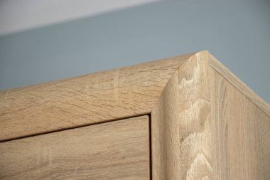 Tahta bir mobilya köşesine yakın çekim, doğal tahıl desenleri sergiliyor. Bu fotoğraf, işçiliğin güzelliğini ve modern iç mekanlardaki ahşabın sıcaklığını yansıtıyor..