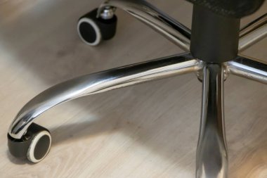 Döner sandalyenin metalik tabanı ve tekerlekleri ahşap zemine yakın plan modern tasarım ve ofis alanları için işlevsellik sergiliyor..