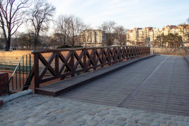 Ağaçlar ve binalarla çevrili bir parktaki ahşap köprü boş zaman ve eğlence için yeşil alana erişim sağlıyor..