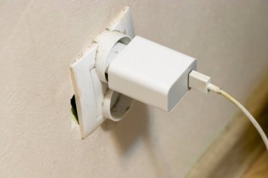 Elektrik prizine takılı beyaz bir şarj aletinin, günlük hayatta teknolojinin önemini vurgulayan bir duvara yakın plan.