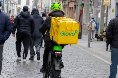 Wroclaw Polonya - 23 Şubat 2025: Glovo dağıtım sürücüsü hareketli bir şehir ortamında yayalarla kalabalık bir caddede geziniyor.