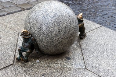 Wroclaw Polonya - 23 Şubat 2025: Wroclaw 'da bir kaldırım taşı caddesinde büyük bir granit topla mücadele eden bir cücenin bronz heykeli. Sanat kültürü turizmi.