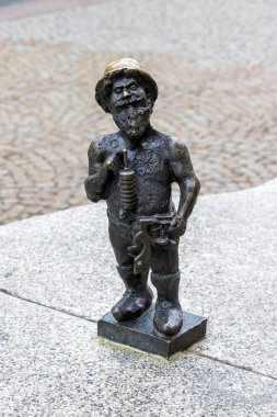 Wroclaw Polonya - 23 Şubat 2025: Garip bir bronz cüce heykeli kaldırımlı bir caddeye karşı bir alet seti taşıyan yerel kültür ve çekiciliği somutlaştıran.