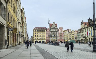 Wroclaw Polonya - 23 Şubat 2025: Wroclaw 'daki renkli binalarla çevrili kalabalık canlı pazar meydanında yürüyor. Bulutlu bir günde canlı bir atmosfer..