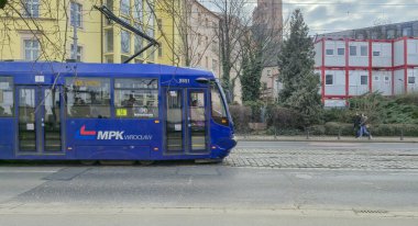 Wroclaw Polonya - 23 Şubat 2025: MPK tramvayı canlı bir şehirde kentsel taşımacılığı gözler önüne seren cadde boyunca konut binalarının önünden geçiyor.