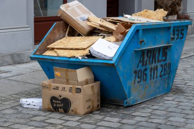 Wroclaw Polonya - 23 Şubat 2025: Karton kutular ve atık maddelerle dolu mavi çöp bidonu binaların yakınındaki bir kaldırım taşı sokakta