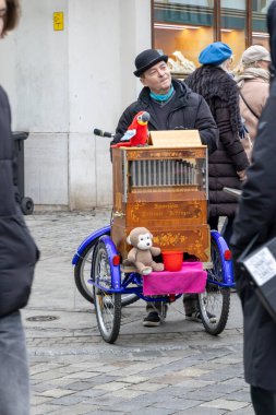Wroclaw Polonya - 23 Şubat 2025: Sokak müzisyeni elle kumandalı bir org eşliğinde renkli oyuncaklar sergiliyor ve yoldan geçenleri canlı bir şehir atmosferine çekiyor.