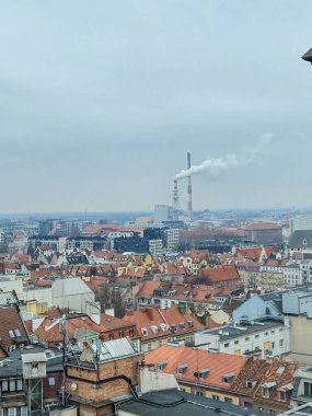 Wroclaw Polonya - 23 Şubat 2025: Wroclaw şehrinin panoramik görüntüsü konut çatılarının ortasındaki fabrika bacalarından çıkan duman endüstriyel bir atmosfer yaratıyor.