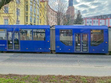 Wroclaw Polonya - 23 Şubat 2025: Canlı bir mahallede şehir ulaşımını gösteren modern mavi bir tramvay şehir caddesi boyunca ilerliyor.