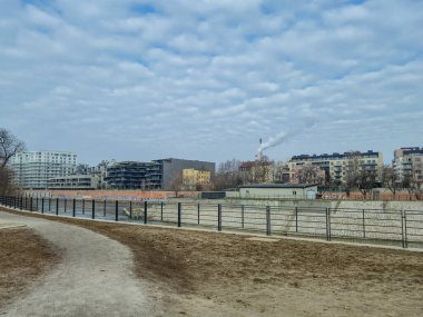 Wroclaw Polonya - 23 Şubat 2025: Bulutlu bir gökyüzü altında modern binalar ve sanayi yapılarının yer aldığı nehir kenarı manzarası.