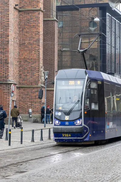 Wroclaw Polonya - 23 Şubat 2025: Canlı bir şehirde şehir ulaşımını bekleyen yolcularla yoğun bir durağa gelen modern bir tramvay