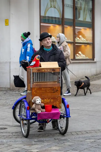 Wroclaw Polonya - 23 Şubat 2025: Bir sokak sanatçısı yayalar ve canlı atmosfer yaratan bir köpekle dolu kalabalık bir sokakta renkli bir müzik kutusu çalıyor.