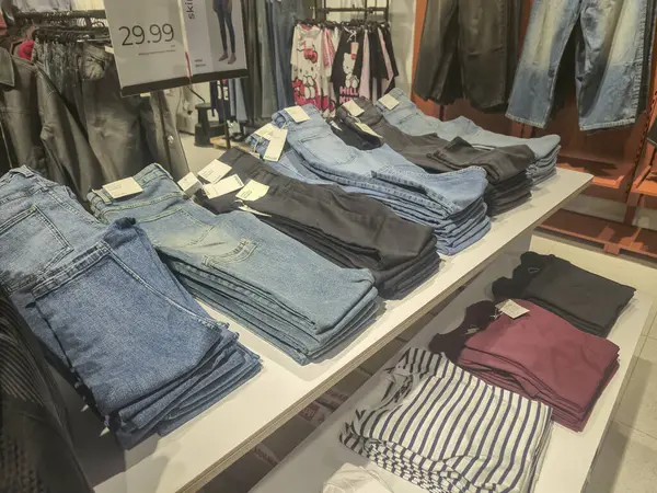 Przemysl Poland - Mart 12025: Bir giyim mağazasında satılık çeşitli renk ve stillerin sergilendiği düzgünce istiflenmiş kot pantolon görüntüsü.