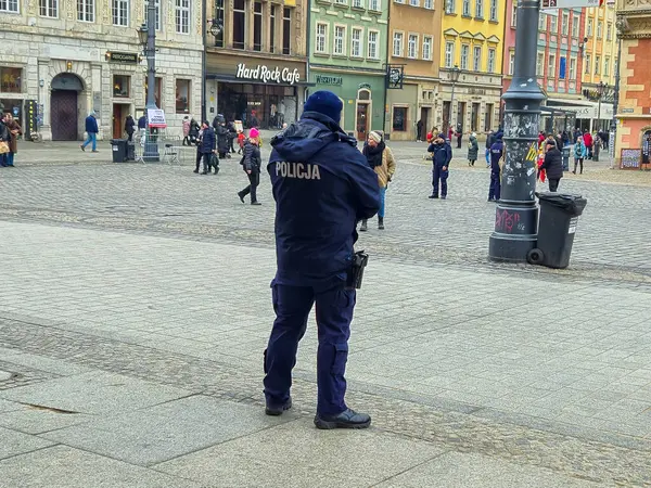 Wroclaw Polonya - 23 Şubat 2025: Polis memuru kış boyunca şehir merkezinde bir meydanı gözlüyor. Vatandaşlar çeşitli faaliyetlerde bulunuyorlar..