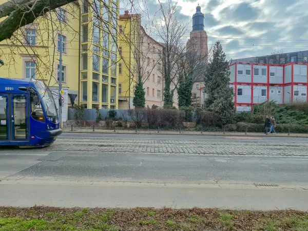 Wroclaw Polonya - 23 Şubat 2025: Yaya geçitlerinde modern ve geleneksel binalarla çevrili bir şehir caddesinde mavi bir tramvay çalışıyor.