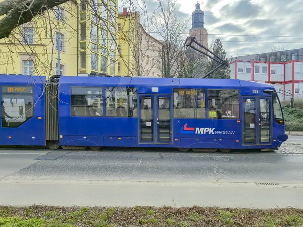 Wroclaw Polonya - 23 Şubat 2025: MPK Wroclaw 'ın mavi tramvayı arka planda ağaçlar ve binalar ile cadde boyunca park edilmiştir.