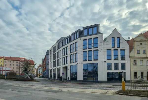 Wroclaw Polonya - 23 Şubat 2025: Bulutlu gökyüzü ile işlek cadde kavşağında büyük cam pencereli modern bina.