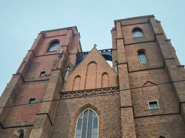 Wroclaw Polonya - 23 Şubat 2025: Bulutlu bir gökyüzü altında kırmızı tuğla mimari ile yüksek kilise cephesinin ayrıntılı bir görüntüsü.