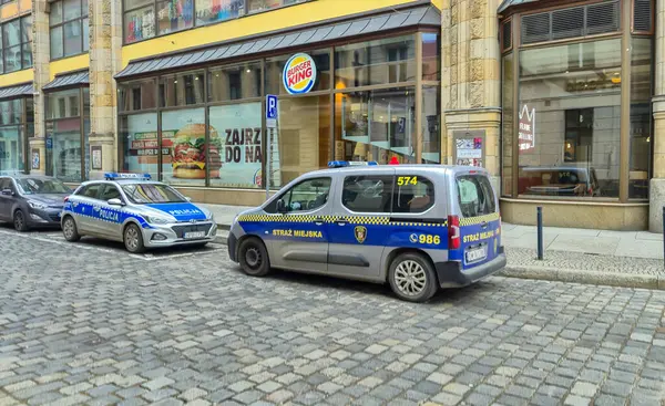 Wroclaw Polonya - 23 Şubat 2025: Bir Burger King restoranının yakınındaki kaldırım taşı caddesinde park halindeki iki polis aracı şehir hayatını ve güvenliğini gözler önüne serdi.