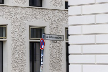 An der Kommandantur 'un sokak tabelası şehir merkezinde eşsiz desenli duvarları olan çağdaş bir binanın yanındaki direğe yerleştirilmiş..
