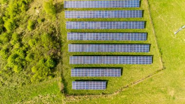 Yeşil çimenlerdeki sıra sıra güneş panelleri ile sürdürülebilir enerji çözümleri gösteren bir güneş çiftliğinin havadan görünüşü. Bu ayar doğal bir ortamda yenilenebilir enerji teknolojisini temsil ediyor..