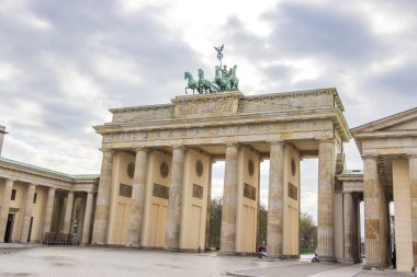 Brandenburg Kapısı Berlin 'de birlik ve barışı simgeleyen bulutlu bir gökyüzünün altında görkemli bir şekilde duruyor. Mimari güzelliklerin sergilendiği popüler bir turistik cazibe..