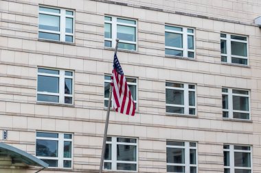 Amerikan bayrağı, vatanseverliği sembolize eden modern bir binanın önünde belirgin bir şekilde sergileniyordu. Çağdaş mimaride büyük pencereler ve şehir manzarasını geliştiren parlak bir cephe yer almaktadır..