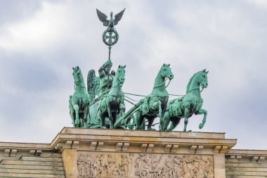 Berlin 'deki Brandenburg Kapısı' nda bir at arabasının tepesinde bronz bir kuadriga heykeli bulunuyor. Sahne, bulutlu gökyüzünün ortasında tarihi bir anlam yakalıyor..