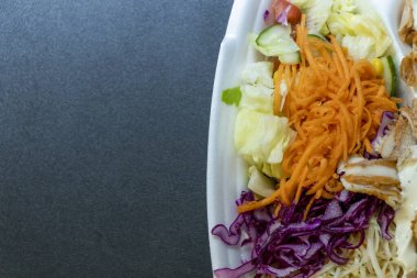 Tek kullanımlık konteynırda taze salata malzemelerinin rengarenk karışımı. İçinde lahana havuçları ve marul var. Öğle yemeği ya da piknik için sağlıklı yemek seçenekleri için ideal..