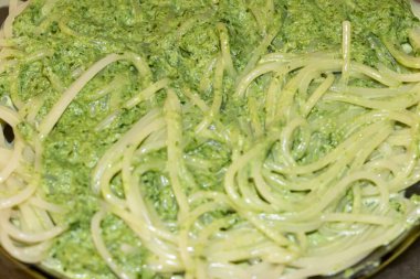 Lezzetli spagetti, canlı yeşil fesleğen sosunun içine atılmış taze bir İtalyan yemeği sergileniyor. Yemek sevenler ve aşçılar için mükemmel servis ediliyor..