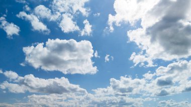 Pofuduk beyaz bulutları etrafa saçılmış parlak mavi gökyüzü açık hava ayarları ve rahatlama için ideal sakin bir atmosfer yaratıyor. Doğa temalı projeler için mükemmel.