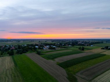 Gün batımında hava manzaralı kırsal alan tarlaları ve küçük köyler üzerinde gökyüzünde canlı renkler sergiliyor. Zengin tarım arazisi olan sakin kırsal alan.