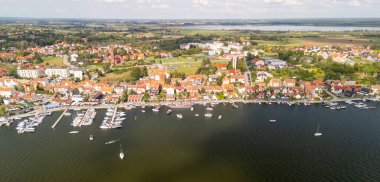 Mazury Polonya 'da büyüleyici bir göl kasabasının havadan görünüşü renkli evler sergiliyor açık gökyüzü altında tekneleri ve manzaralı yeşillikleri olan bir marina.
