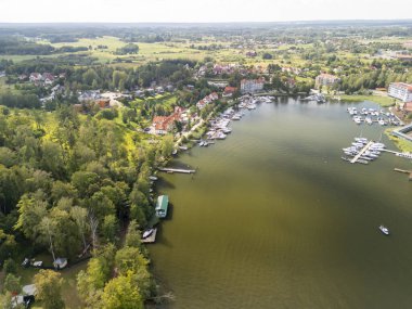 Mazury Polonya 'da yeşil ormanlar ve renkli evlerle çevrili hava manzaralı göl manzarası huzurlu yaz doğa aktivitelerini ve canlı doğa aktivitelerini sergiliyor..