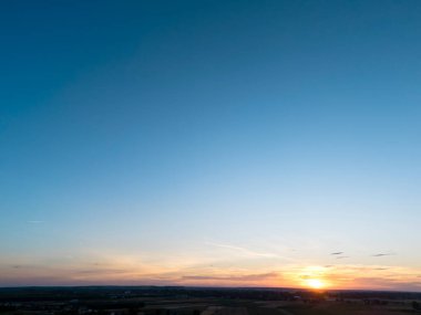 Huzurlu bir manzara üzerinde çarpıcı bir gün batımı gökyüzünde canlı renkler ve aşağıdaki dingin alanlar huzur ve güzelliği çağrıştırıyor..
