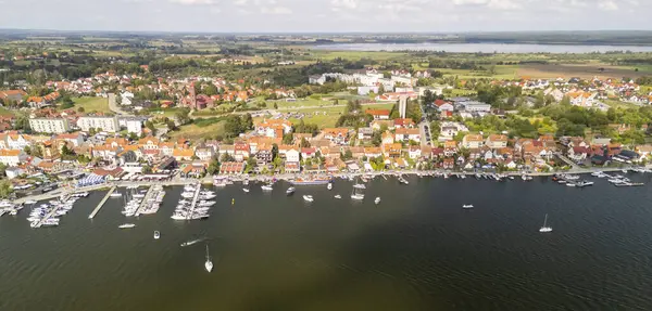Mazury Polonya 'da büyüleyici bir göl kasabasının havadan görünüşü renkli evler sergiliyor açık gökyüzü altında tekneleri ve manzaralı yeşillikleri olan bir marina.