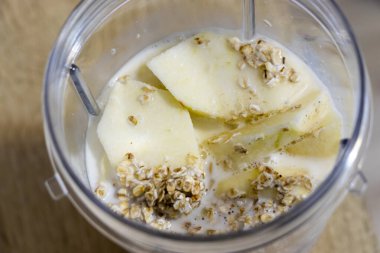 Doğranmış yeşil elma yulafı ve sütle dolu bir mikserin yakın çekimi kahvaltı ve beslenme için ideal bir içecek hazırlıyor..