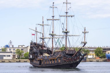 Gdynia Polonya - 17 Haziran 2022: Modern binalar ve yeşil ağaçlarla çevrili tarihi bir korsan gemisi limandan geçiyor.