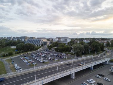 Rzeszow Polonya - 3 Haziran 2024: Yoğun bir otoyol parkı ve parçalı bulutlu gökyüzü altındaki modern binaların yer aldığı şehir manzarası.