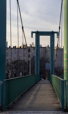 Wroclaw Polonya - 23 Şubat 2025: Günbatımında modern bir yaya asma köprüsü kent mimarisini gözler önüne seriyor.