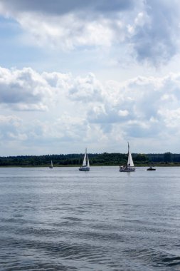 Mikolajki Polonya - 29 Eylül 2024: Bulutlu bir gökyüzü altında sakin sularda süzülen yelkenlilerin manzarası barışçıl ve sakin bir atmosfer yaratıyor.