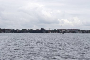 Mikolajki Polonya - 29 Eylül 2024: Bulutlu bir gökyüzü altında küçük bir tekne ve göl binaları bulunan bir gölün manzarası sakin bir atmosferi yakalıyor.