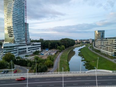 Rzeszow Polonya - 3 Haziran 2024: Günbatımında bulutlu bir gökyüzünün altında nehir ve parka sahip modern mimarinin manzarası.