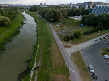 Rzeszow Polonya - 3 Haziran 2024: Rzeszow 'da bisikletli yayalar ve yol boyunca yemyeşil otlakların yer aldığı sakin bir nehir kıyısının havadan görünüşü.