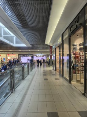 Przemysl Polonya - Mart 12025: İnsanlarla dolu bir alışveriş merkezi koridorunun geniş bir görüntüsü. Perakende mağazaları duvarlarda çeşitli marka ve ürünleri sergiliyor..