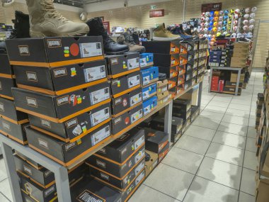 Przemysl Polonya - Mart 12025: Taktik ve açık hava çizmeleri de dahil olmak üzere çeşitli ayakkabı giyim seçeneklerini renkli kutularla raflarda gösteren bir ayakkabı mağazası.