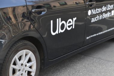 Berlin Almanya - 11 Nisan 2025: Bir şehir caddesinde park halindeyken logoyu ve markasını gösteren bir Uber aracının yakın çekimi.