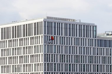 Berlin Almanya - 11 Nisan 2025: PWC logosunun yer aldığı modern ofis binası şık mimari sergileniyor ve bulutlu bir gökyüzüne karşı cam cephe.