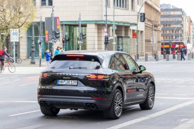 Berlin Almanya - 11 Nisan 2025: Gösterişli siyah bir Porsche Cayenne SUV, yayalar ve bisikletçiler arasında lüks ve şehir yaşamını harmanlayan şehir trafiğinde manevra yaparken yakalandı.