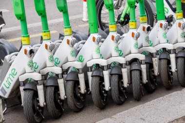 Berlin Almanya - 11 Nisan 2025: Canlı yeşil ve beyaz renkli kentsel hareketlilik seçeneklerini gösteren bir dizi elektrikli scooter şehrin caddesinde park etti.